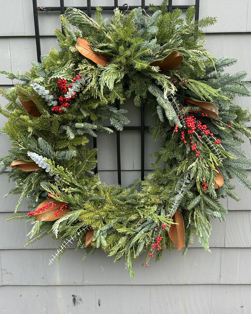 Handmade fresh evergreen wreath with magnolia leaves and red winterberry